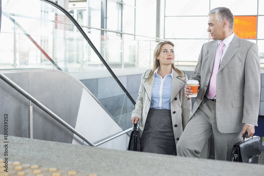 Businessman conversing with female colleague while walking up stairs in train station Businessman conversing with female colleague while walking up stairs in train station