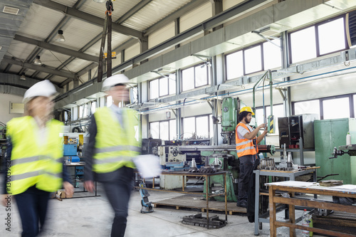 Blurred motion of business people with manual worker in background at industry