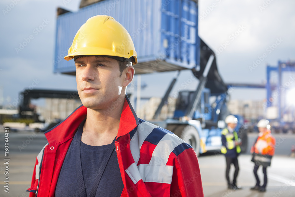 Confident male worker with colleagues in background at shipping yard Confident male worker with colleagues in background at shipping yard