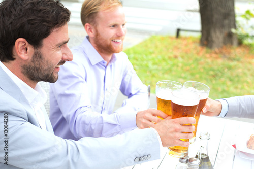 Businessmen toasting beer glasses with female colleague at outdoor restaurant