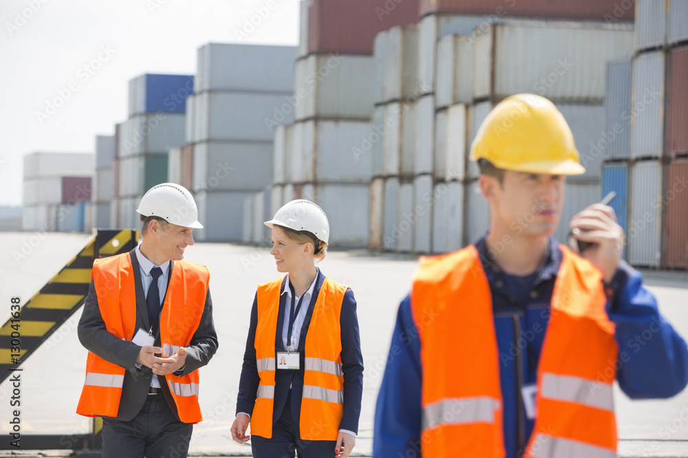 Worker using walkie-talkie while colleagues discussing in shipping yard Worker using walkie-talkie while colleagues discussing in shipping yard