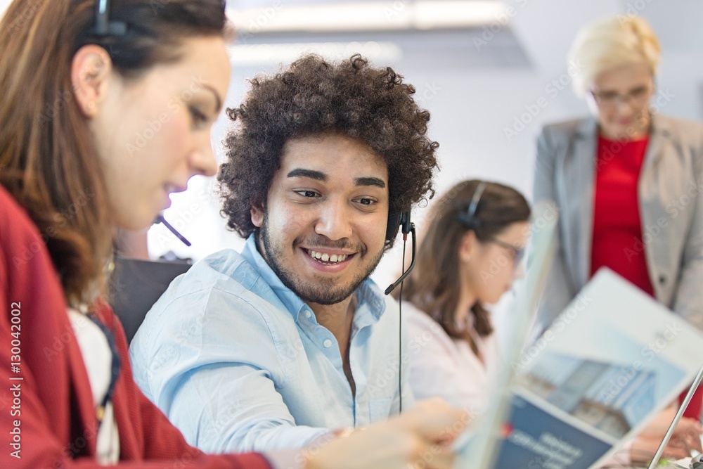 Young businessman discussing with businesswoman with colleagues in background at office Young businessman discussing with businesswoman with colleagues in background at office
