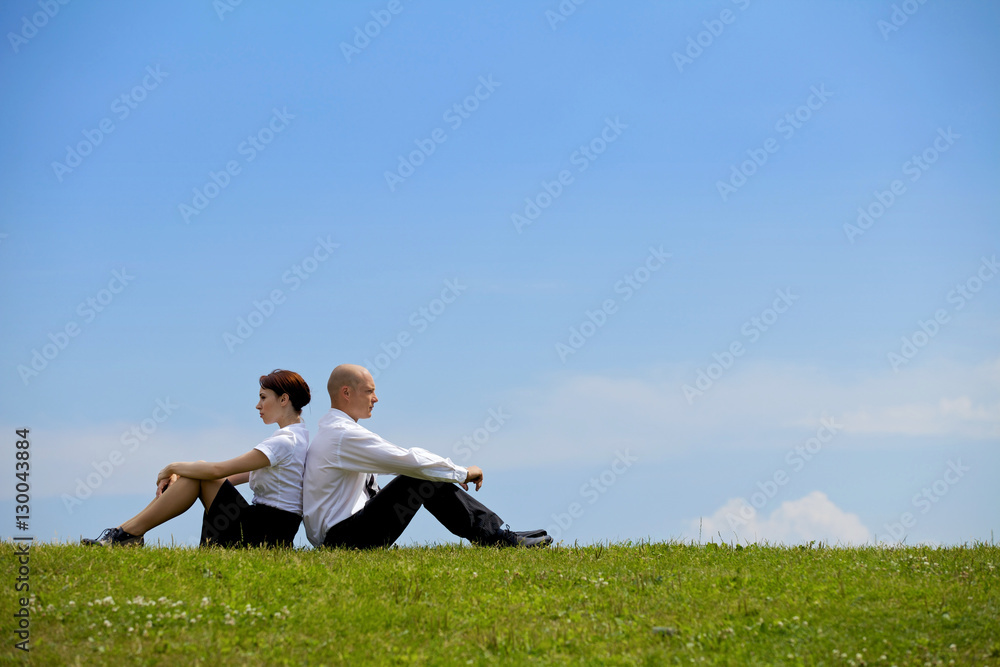 Business couple sitting back to back on grass Business couple sitting back to back on grass