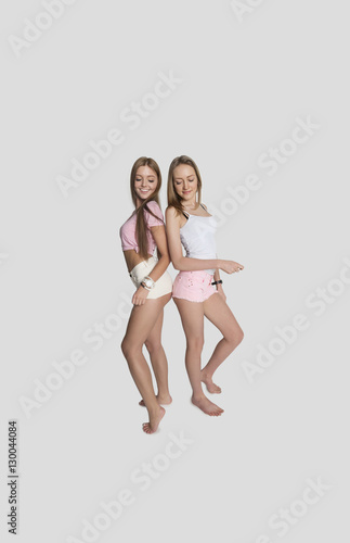 Full length of female friends wearing hot pants posing over gray background