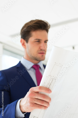 Confident young businessman analyzing blueprint in new office