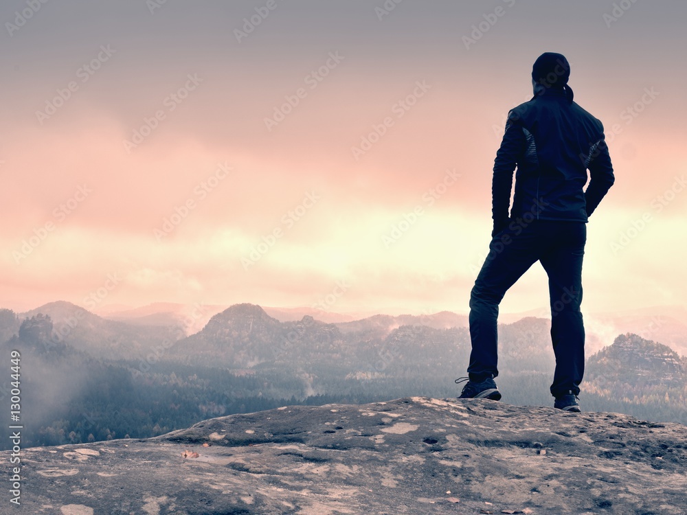 Hiker on rock end above valley. Man watch over misty and foggy valley Hiker on rock end above valley. Man watch over misty and foggy valley