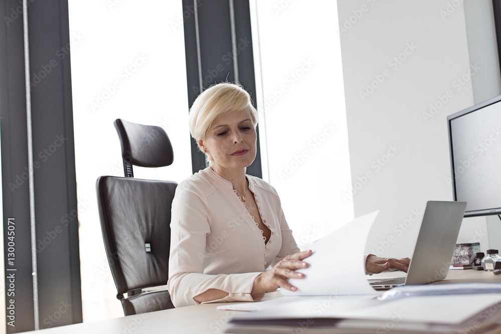 Mature businesswoman reading document at desk in office Mature businesswoman reading document at desk in office