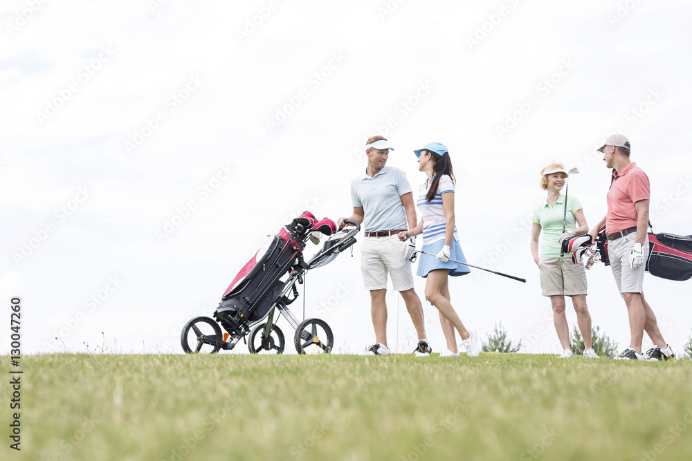 Friends communicating while walking at golf course against clear sky Friends communicating while walking at golf course against clear sky