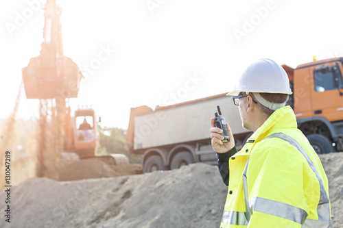 Side view of supervisor using walkie-talkie at construction site against clear sky photo