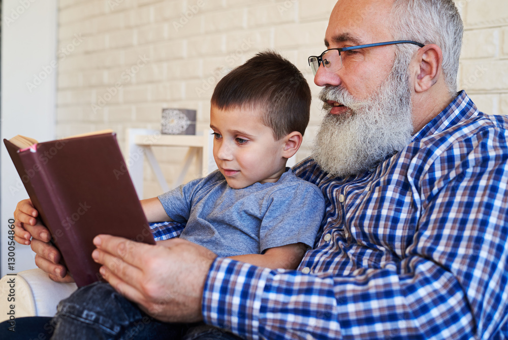 A senior grandfather and his grandson reading attentively an int A senior grandfather and his grandson reading attentively an int