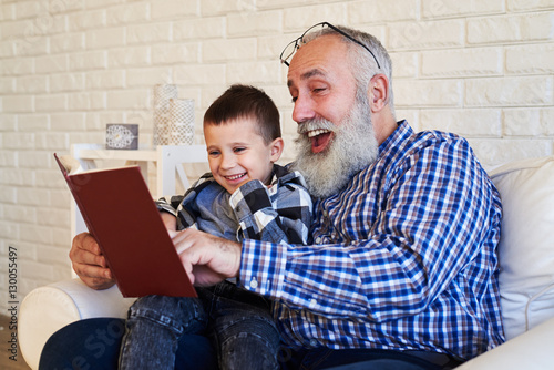 фотографія Mid side shot of elated granfather and his son while reading a s