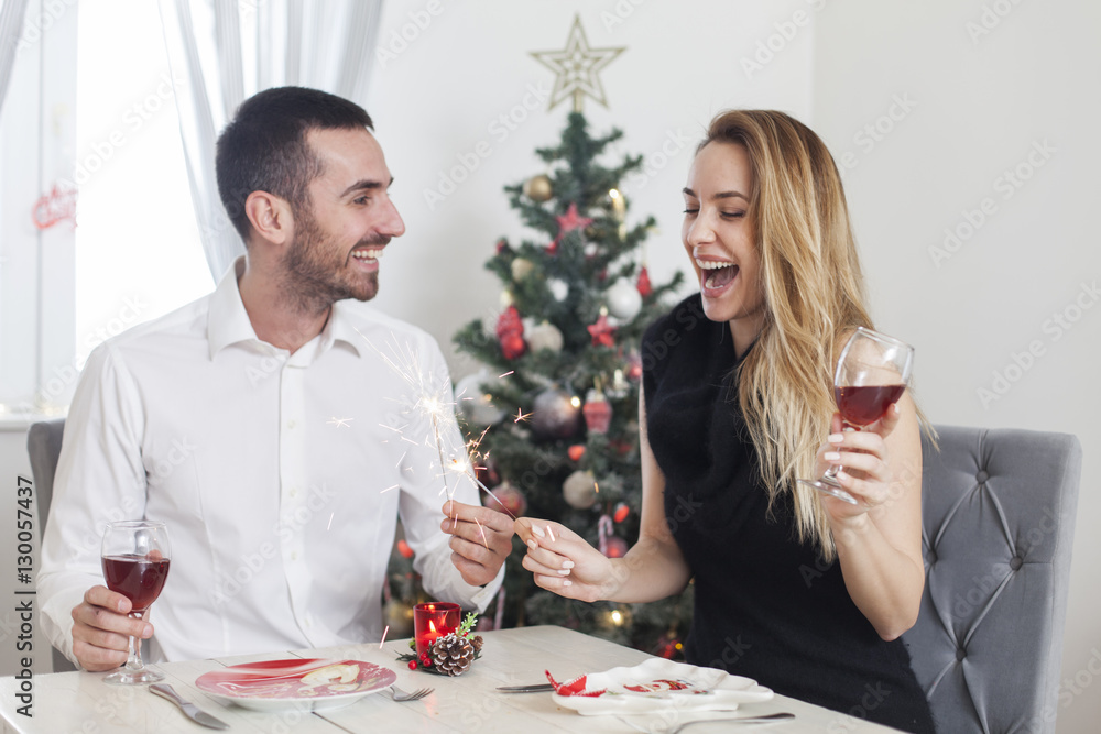 Young beautiful happy couple having a Christmas dinner holding fireworks sticks. New Years dinner