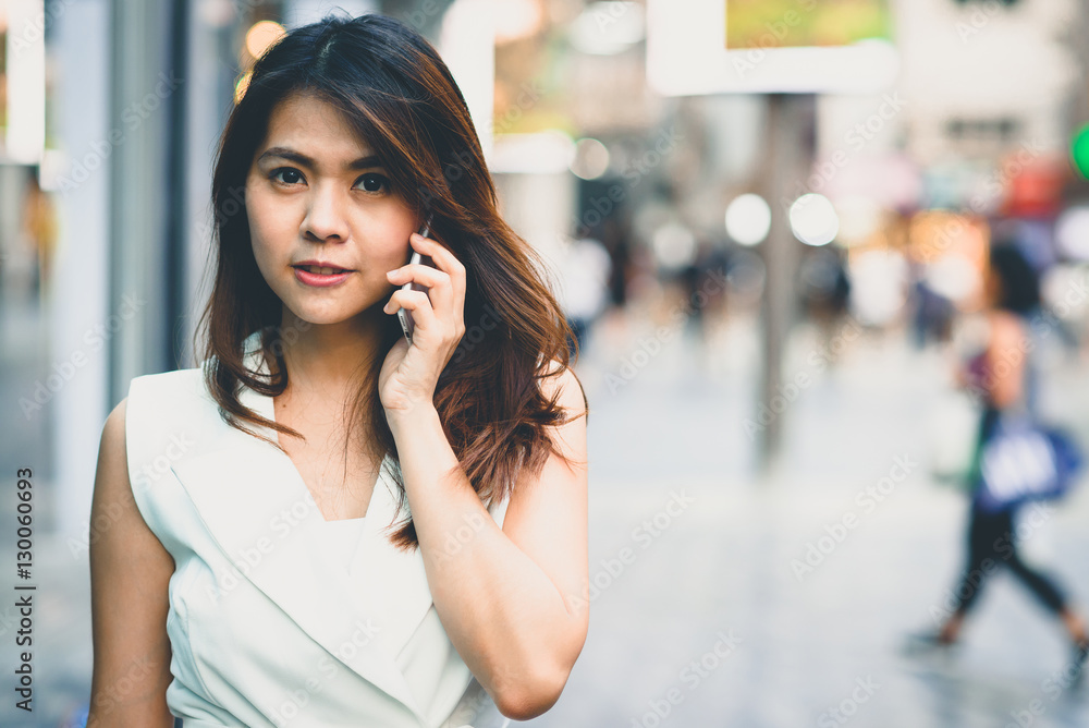 Portrait of young beautiful Asian woman talking on smartphone with people in city street background. Vintage tone image. Portrait of young beautiful Asian woman talking on smartphone with people in city street background. Vintage tone image.
