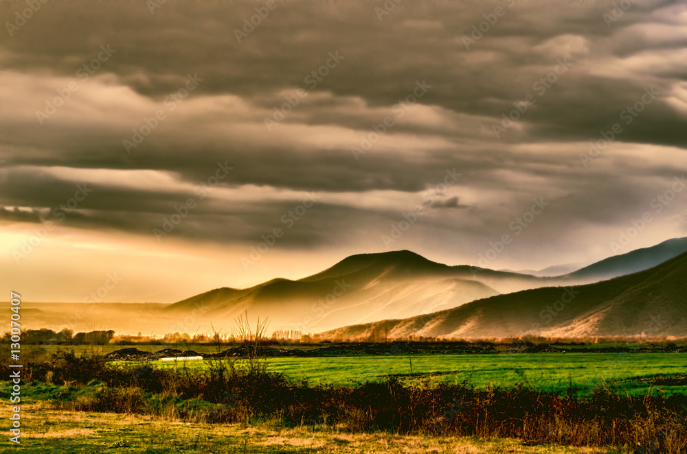 Sunset in green field, mountains, sky and  clouds as background