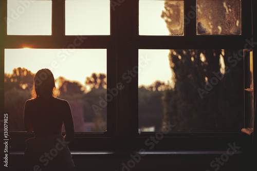 Beautiful naked woman sitting on a window at sunset