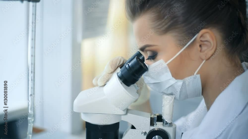 Female scientist looking through a microscope in laboratory Female scientist looking through a microscope in laboratory