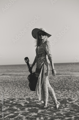 Beautiful woman playing guitar on the beach at sunset outdoors background
