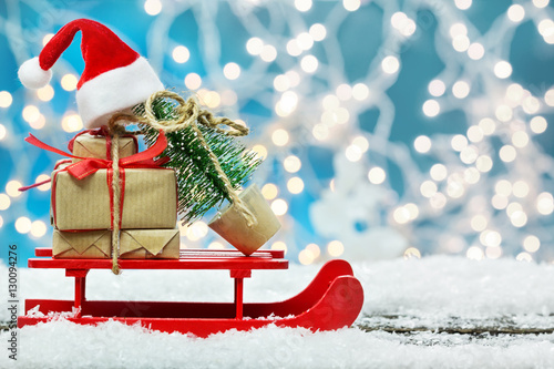 Weihnachtsgeschenke und Tannenbaum mit Weihnachtsmütze auf Schlitten  photo