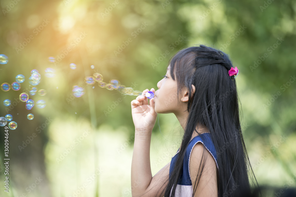 Cute little girl wearing a blue and white dress blowing bubbles in the park,vintage style.