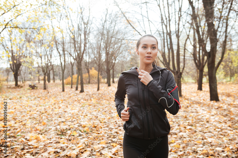 Young lady runner in warm clothes and earphones running Young lady runner in warm clothes and earphones running