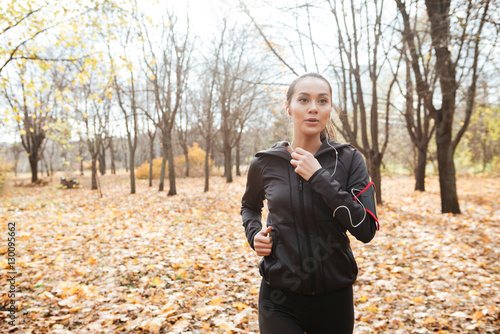 Young lady runner in warm clothes and earphones running