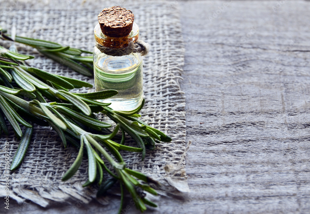 Rosemary essential oil in a glass bottle with fresh green rosemary herb on old wooden table.Rosemary oil for spa,aromatherapy and bodycare.Extract oil of rosemary.Selective focus.Copy space. - obrazy, fototapety, plakaty 