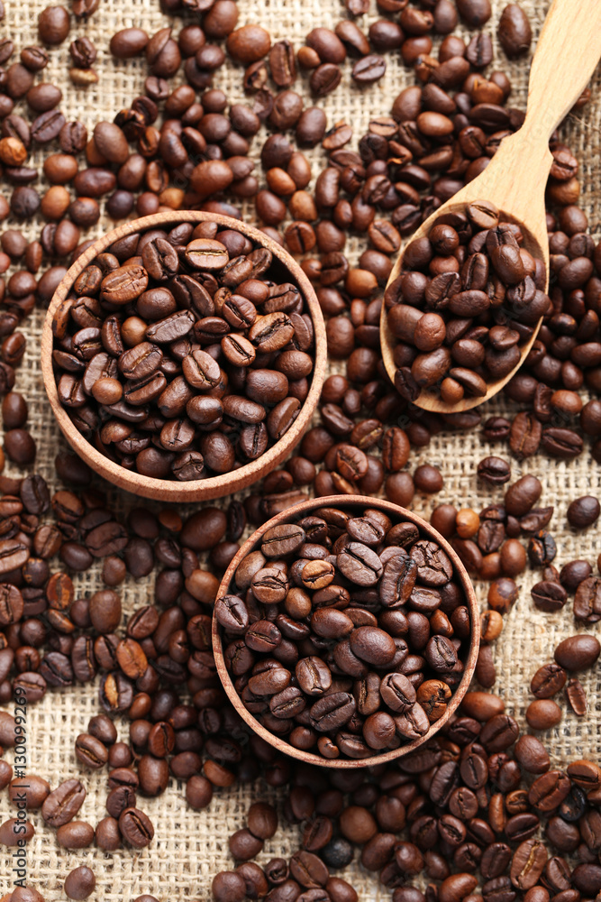 Fototapeta premium Brown roasted coffee beans in bowl on sackcloth