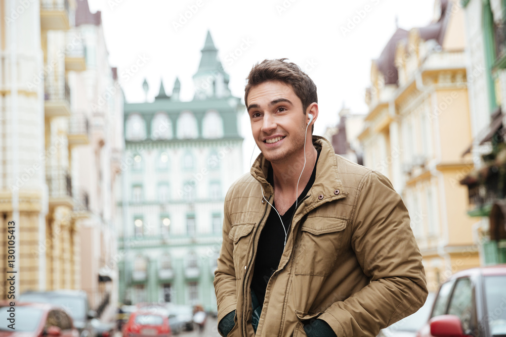 Young cheerful man walking on the street and looking aside.