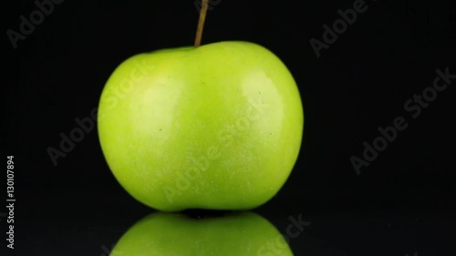 Rotating green apple and its reflection on a black background.