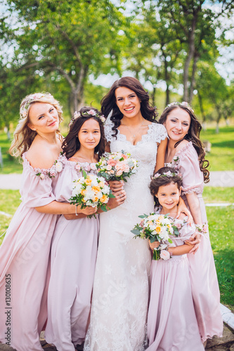 Bride with bridesmaids and little girl kids in the same color dress posing on camera in the park on the wedding day