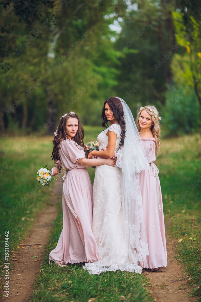Wedding. The bride in a white dress standing and embracing bridesmaids in green and yellow garden park or forest.