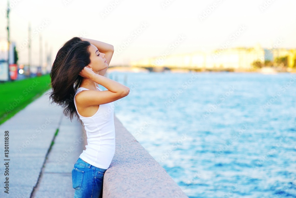 Portrait of beautiful slender brunette girl straightens her long hair with his hands, standing on the promenade at sunset Portrait of beautiful slender brunette girl straightens her long hair with his hands, standing on the promenade at sunset