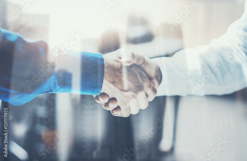 Double exposure concept.Close up view of business partnership handshake .Photo two businessman handshaking process.Skyscraper office building on the blurred background.Horizontal,film effect.