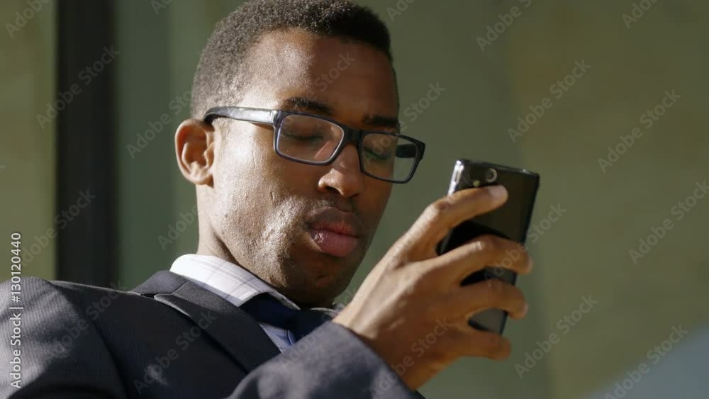 handsome African-american businessman texting messages on his smartphone handsome African-american businessman texting messages on his smartphone