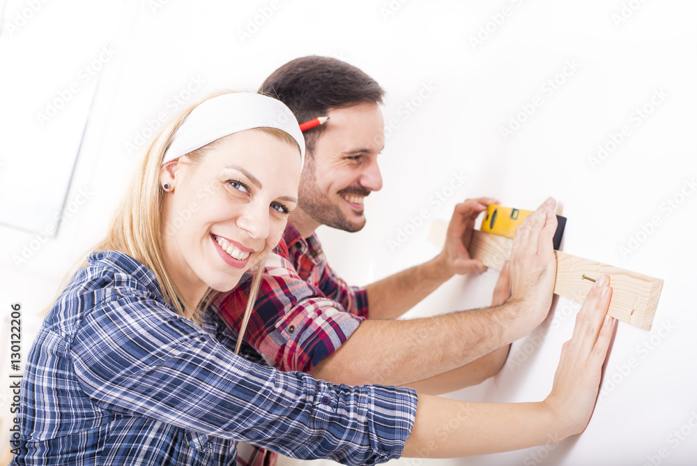 Young couple mounting wood shelf and doing repair at home together Young couple mounting wood shelf and doing repair at home together