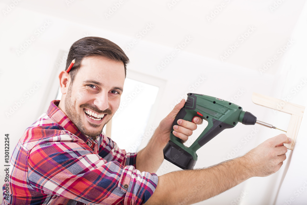 Young smiling man mounting wood shelf and doing repair at home