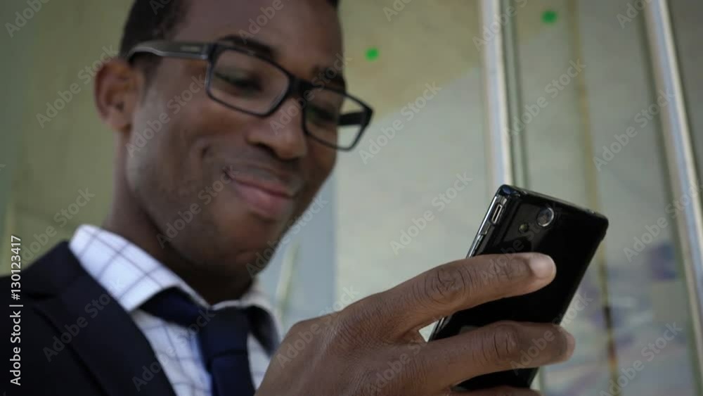 handsome black businessman reads a message on the smartphone and smiles handsome black businessman reads a message on the smartphone and smiles