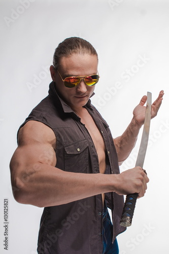 Portrait of a brutal man bodybuilder in sunglasses with a sword on a white background photo