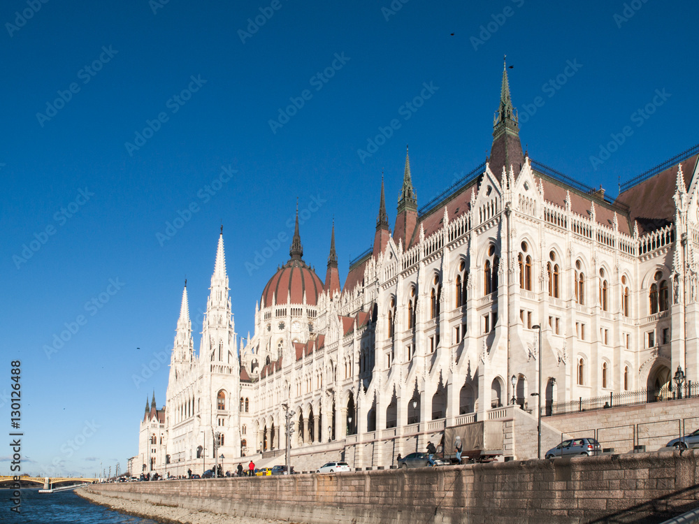 Fototapeta premium Daytime view of historical building of Hungarian Parliament, aka Orszaghaz, with typical symmetrical architecture and central dome on Danube River embankment in Budapest, Hungary, Europe. It is