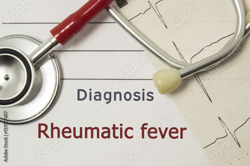 Cardiac diagnosis of Rheumatic fever. On doctor workplace are red stethoscope, printed on paper ECG line and a pen close up lying on medical handbook, which indicated diagnosis of Rheumatic fever