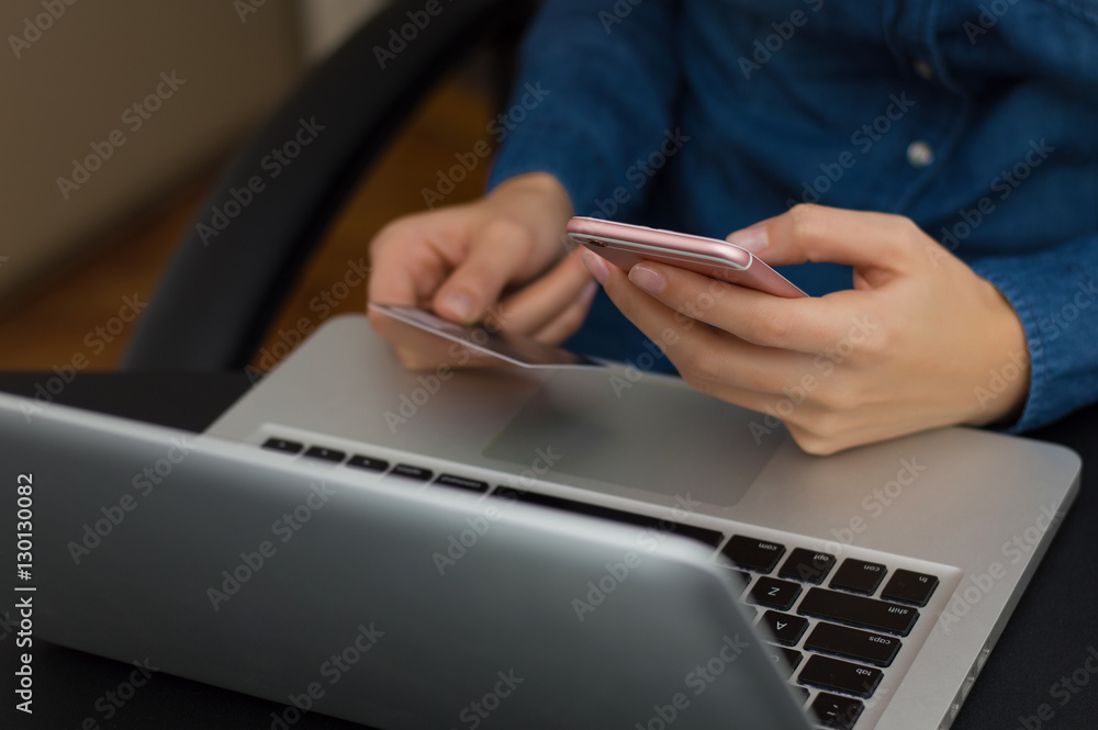 Fototapeta premium Female holding credit card while using laptop and cellphone on w