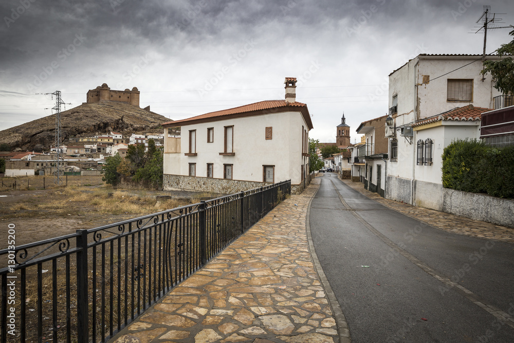 a street in La Calahorra town and the ancient Castle-Palace on a cloudy day, Province of Granada, Spain