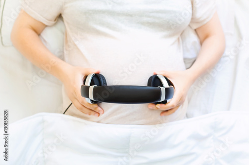 Pregnant young woman with headphones on her belly