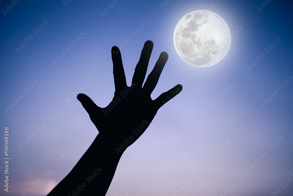 Silhouette of a hand with full moon on fantastic sky background.