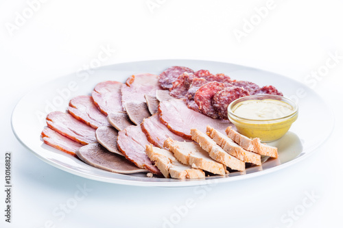 Assorted meat: ham, smoked sausage, salami, chicken, tongue and mustard on a white background