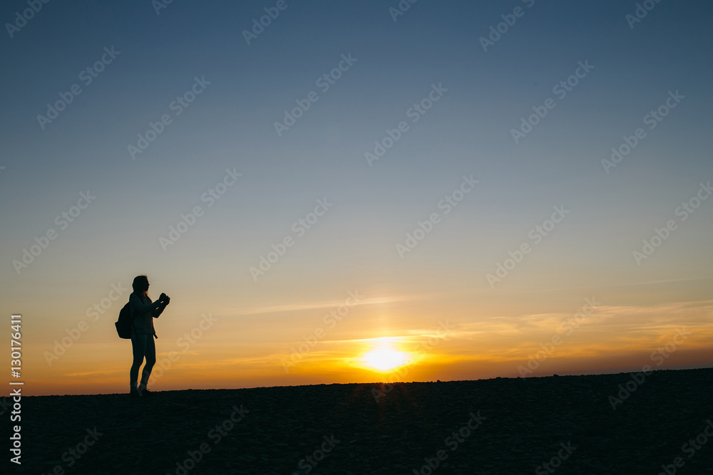 silhouette of a young woman taking pictures on the camera at sunset background