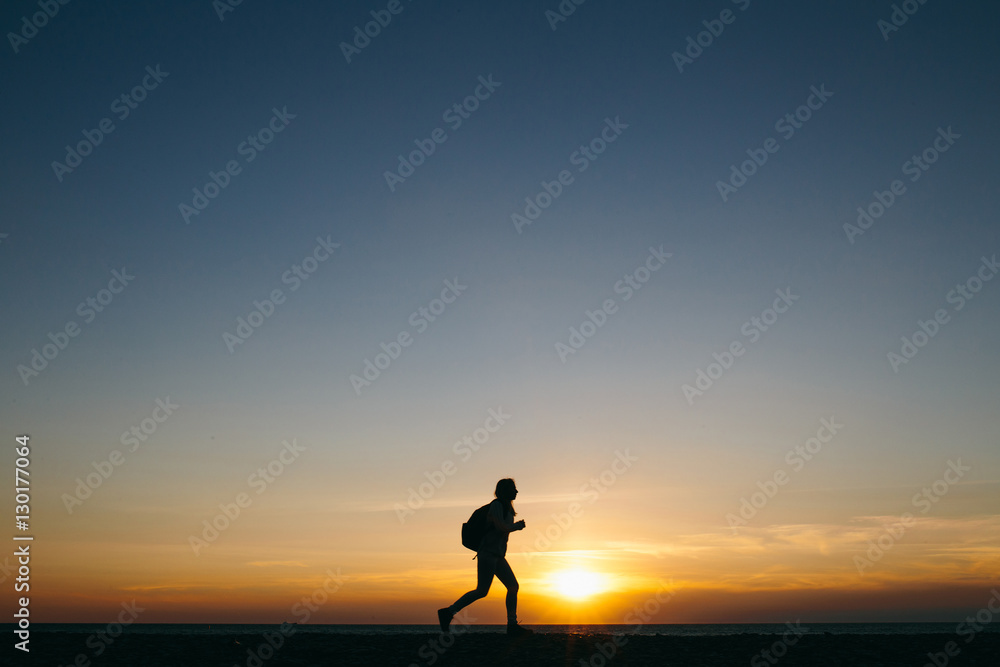 silhouette of a running young woman traveler on sunset sky background