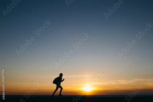 silhouette of a running young woman traveler on sunset sky background