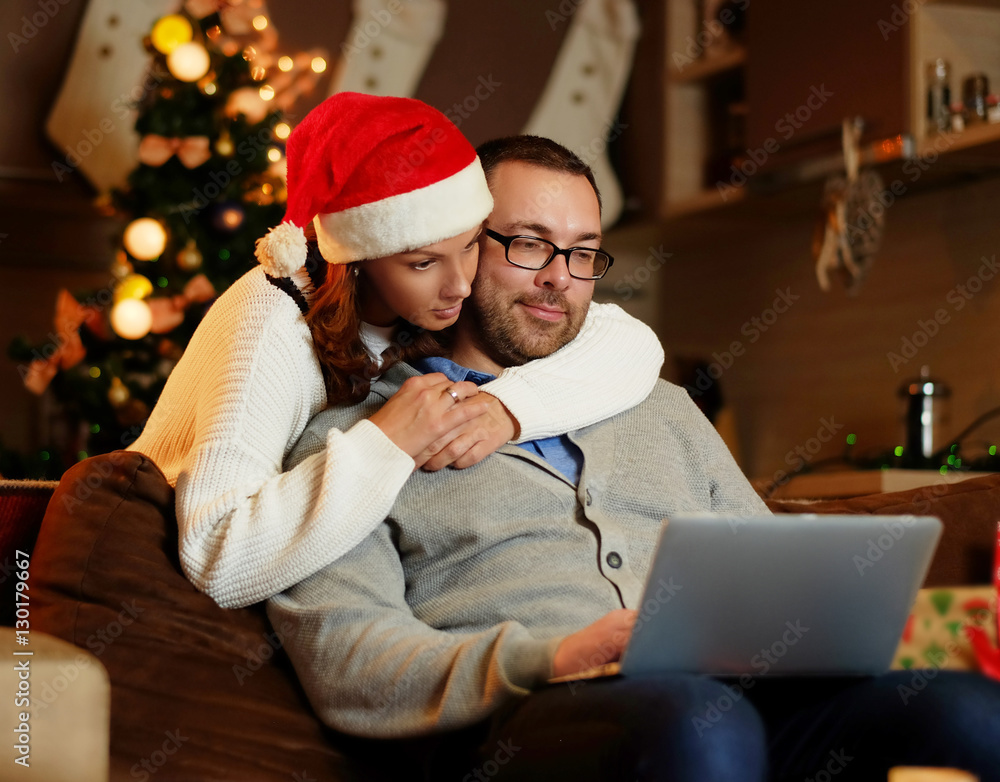 Christmas holiday. Female in Santa's hat hugging a man using a l Christmas holiday. Female in Santa's hat hugging a man using a l
