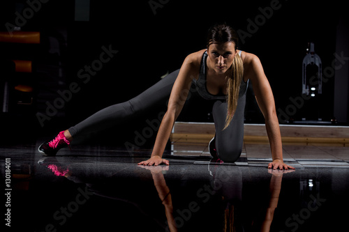 woman in a gym exercising, doing push ups. Dark background
